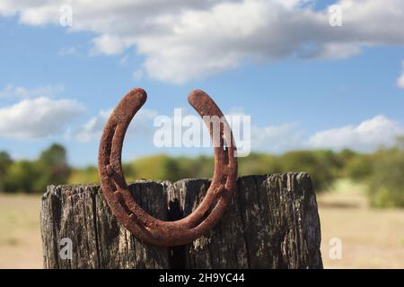 Metall-Hufeisen auf Holzpfosten mit blauem Himmel und flauschigen Wolken Stockfoto