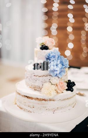 Dreistufiger Kuchen mit Blumen und Beeren verziert steht auf einem weißen Ständer auf dem Tisch Stockfoto