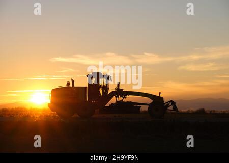 Silhouette eines schweren Traktors, der bei Sonnenuntergang auf der Straße fährt. Stockfoto