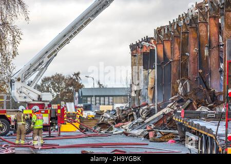 Kidderminster, Großbritannien, 8th. Dezember 2021. Feuerwehrleute und Polizei sind immer noch beim Lagerfeuer auf dem Hoo Farm Industrial Estate, Kidderminster. Die Überreste des Gebäudes von MCD werden noch 48 Stunden nach Beginn des Feuers mit Wasser übergossen. Rauch und kleine Brände sind immer noch offensichtlich, da die Feuerwehr nun die Kontrolle über die Situation hat. Kredit: Lee Hudson Stockfoto