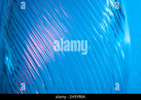 Abstrakter Glashintergrund. Textur aus gewelltem Glas, beleuchtet mit mehrfarbigem Licht. Rosa und blaue Flecken. Nahaufnahme. Fackeln auf Glas Stockfoto