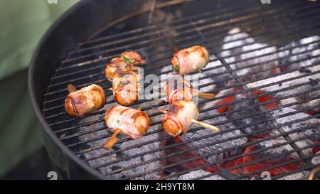 Gegrillte Wurst mit Speck. Würstchen mit Speck auf dem Grill gebraten. Würste in Speck eingewickelt Grill in der Natur zubereitet. Stockfoto