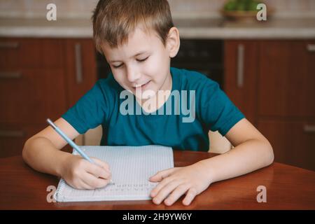 Niedliches Kind Briefe in Notizbuch sitzen am Tisch Stockfoto