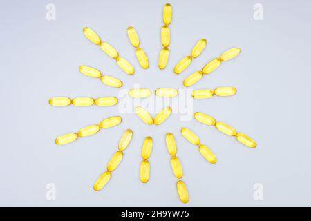 Fischöl-Softgel-Kapseln, die in eine Sonnenform angeordnet sind, isoliert auf einem neutralen Hintergrund. Vitamin D Nahrungsergänzungsmittel. Stockfoto