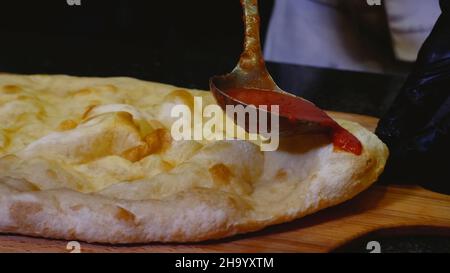 Der Koch gießt Pizza mit Tomatensauce. Rahmen. Aus der Nähe des Küchenchefs gießt eine Kelle Tomatensauce auf die italienische Pizza. Vorbereitung der traditionellen italienischen Pizza. Konz Stockfoto