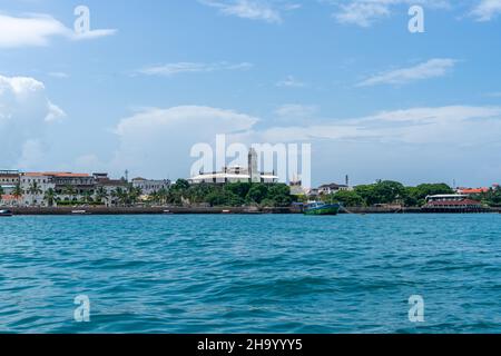 Die Skyline von Stone Town in Sansibar vom Wasser aus gesehen. Sonniger Tag mit Wolken. Reisekonzept mit türkisfarbenem indischen Ozean Stockfoto