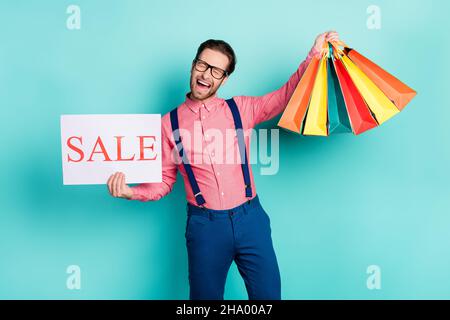 Foto von jungen aufgeregt Mann glücklich Lächeln halten Banner Verkauf shopaholic Taschen isoliert über türkisfarbenen Hintergrund Stockfoto