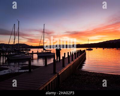 Ein Steg und Segelboote bei Sonnenuntergang in Ambleside, am Lake Windermere, Lake District, Großbritannien. Stockfoto