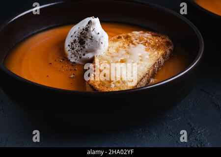 Cremige Butternussuppe mit Creme, Parmesan-Toasts in brauner Keramikschale auf dunkelgrauem Hintergrund, herbstlich gemütliches vegetarisches Gericht Stockfoto