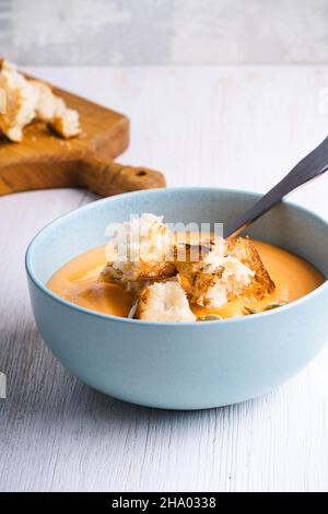 Cremige Butternut-Kürbissuppe mit Brottoast Croutons in blauer Keramikschale auf weißem Holzhintergrund, herbstlich gemütliches veganes Gericht Stockfoto
