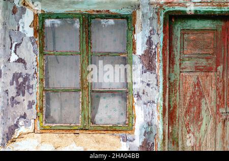 Das Äußere einer alten, rissigen Hauswand mit alten Fenstern und Türen Stockfoto