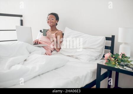 Eine junge Frau mit einem Laptop im Bett zu Hause Stockfoto