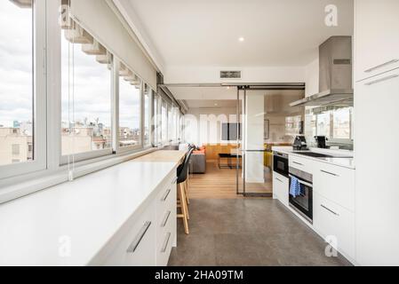 Große Küche mit weißen Schränken und Blick auf die Skyline mit Glastüren in einer Ferienwohnung Stockfoto