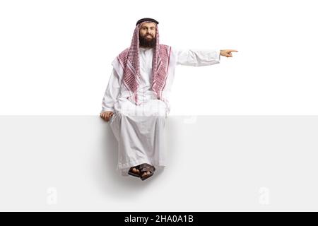 Saudi-arabischer Mann, der auf einer leeren Tafel sitzt und isoliert auf weißen Hintergrund zeigt Stockfoto