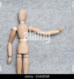 Kleine Holzfigur streckt die Hand aus und zeigt auf etwas vor einem grauen Filzhintergrund. Speicherplatz kopieren. Draufsicht. Stockfoto