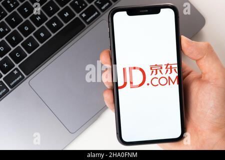 Jingdong Mall mobile Anwendung auf dem Smartphone-Bildschirm. Ein Mobiltelefon in einer Männerhand in der Nähe eines offenen Laptops. Weißer Hintergrund. November 2021, San Francisco, USA Stockfoto