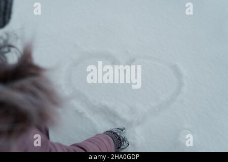 Ein Mädchen in einer rosa Jacke zieht ein Herz in den Schnee, Liebe ist überall um uns herum, Liebe schmilzt Eis Stockfoto