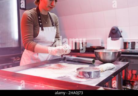 Eine Köchin arbeitet mit einem Teig in der Küche eines Restaurants. Schöne rote Beleuchtung Stockfoto