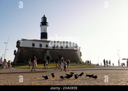 Salvador, Bahia, Brasilien - 29. Juli 2021: Blick von unten auf Farol da Barra in Salvador, mit Tauben, die Mais auf dem Boden fressen und Touristen, die spazieren gehen. Stockfoto