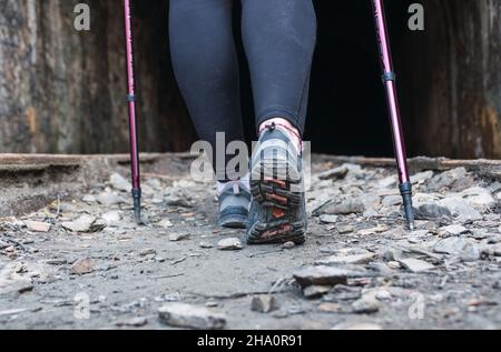 Frau, die auf einem Steinweg mit Wanderschuhen und Stöcken wandert. Frau, die am Eingang eines Tunnels entlang einer alten Eisenbahnstrecke geht. Stockfoto