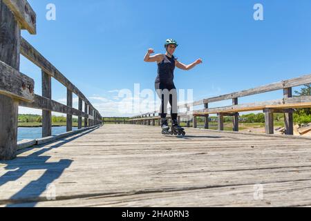Frau wackelt auf Rollerblades am Dock über dem Ozean Stockfoto