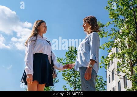 Kaukasisches Schulmädchen mit Rucksack und Uniform hält ihre lächelnde Mutter Stockfoto