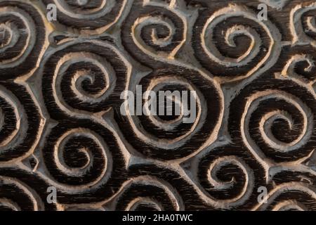 Dunkle Holzplatte mit geschnitztem Spiralornament, Nahaufnahme Stockfoto