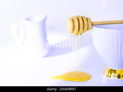 Honig fließt aus gedrehtem Honigstock. Honigs tun auf weißem Hintergrund. Frühstücksahnekännchen Stockfoto