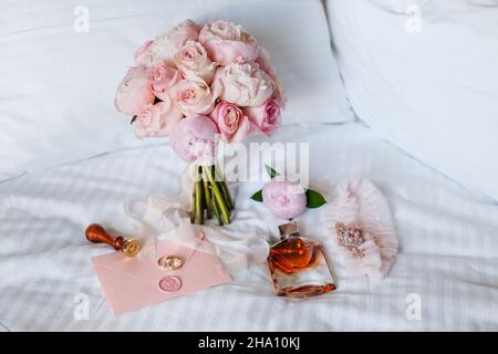 Hochzeitsbraut boutonniere, Bouquet, Duft und Strumpfband auf weißer Bettwäsche. Rosa Brautblumen und Accessoires aus nächster Nähe Stockfoto