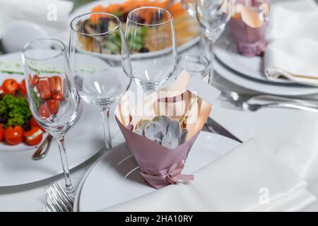 Geschenk für Gäste auf der Hochzeit - leere Einladung Gästekarte und süß Sukculent. Partytisch mit Serviette, Weinläsern, Teller. Rezeptionsdekor im Restauant. Stockfoto