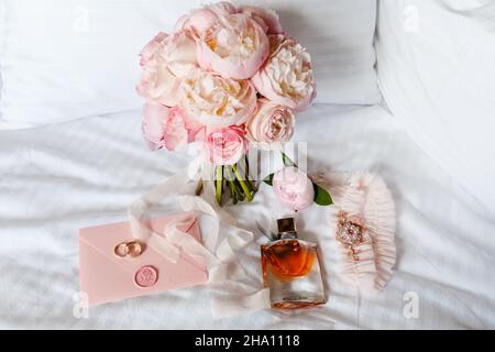 Hochzeitsbraut boutonniere, Bouquet, Duft und Strumpfband auf weißer Bettwäsche. Rosa Brautblumen und Accessoires aus nächster Nähe Stockfoto