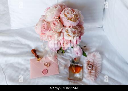 Hochzeitsbraut boutonniere, Bouquet, Duft und Strumpfband auf weißer Bettwäsche. Rosa Brautblumen und Accessoires aus nächster Nähe Stockfoto