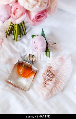 Hochzeitsbraut boutonniere, Bouquet, Duft und Strumpfband auf weißer Bettwäsche. Rosa Brautblumen und Accessoires aus nächster Nähe Stockfoto