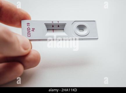 RADT (Rapid Antigen Detection Test) mit einem roten Streifen, der EIN NEGATIVES Ergebnis eines Tests mit menschlicher Probe zeigt. Man-Finger, die den weißen Plastik-de Stockfoto