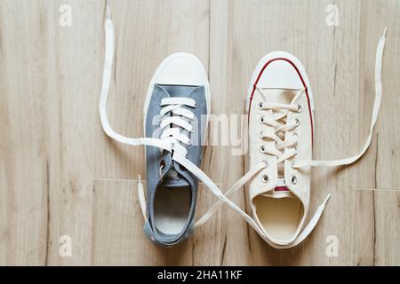 Grau und beige Farbe lässige neue Turnschuhe mit weißen Schnürsenkeln auf dem Holzboden Nahaufnahme Bild verflochten. Liebe und Freundschaft Konzept Bild. Stockfoto