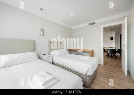 Schlafzimmer mit zwei separaten Betten mit Handtüchern und weißen Schränken, wandfernseher und großem Fenster mit Blick in eine Ferienwohnung Stockfoto