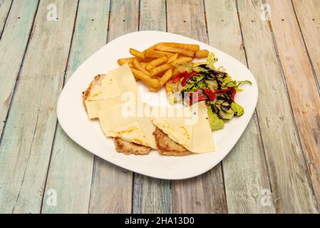 Kombinationsteller aus Schweinelende mit Käse, Pommes frites, Salat mit Paprika, Gurken und Balsamico-Essig auf einem weißen Porzellanteller Stockfoto