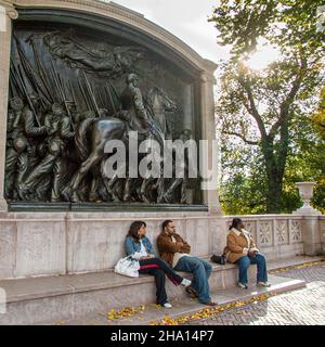 Drei Personen sitzen vor dem Robert Gould Shaw Memorial auf dem Boston Common. Stockfoto