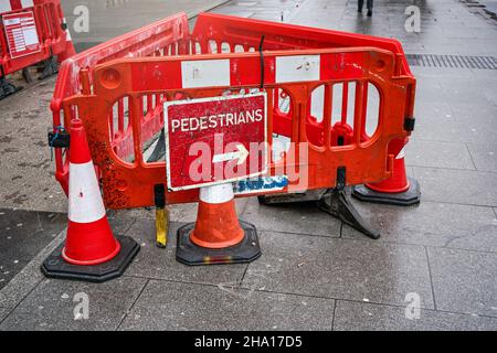 London, Vereinigtes Königreich - 04. Februar 2019: Rote Straßensperre mit einem Pfeilschild, das Fußgänger zum Umherlaufen anleitet, auf nassem Bürgersteig, Verkehrskegel platziert Stockfoto