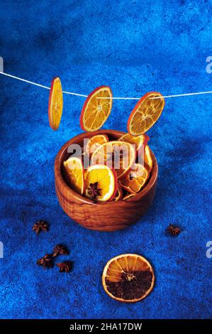 Vertikale Hochwinkelansicht von orangefarbenen Scheiben, die zum Trocknen an Baumwollsträngen hängen. Anissterne und eine einzelne Scheibe, die verbrannt wird. Stockfoto