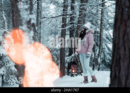 Das Mädchen hält eine Laterne mit einem Licht in der Hand und leuchtet auf ihrem Weg in den gefrorenen Wald, Weihnachten und gefrorene Atmosphäre, Bethlehem Licht leuchtet ich Stockfoto