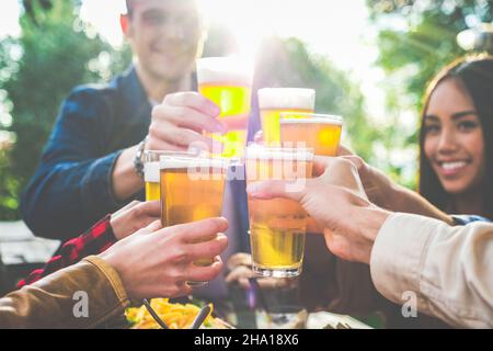 Eine Gruppe von multiethnischen Freunden trinkt Bier im Pub-Restaurant im Freien - Jugendliche genießen während der Happy Hour Getränke an der Terrassenbar beim Toasten Stockfoto