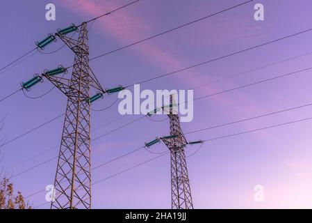 Detail von zwei Strommasten, die Hochspannungskabel in der Abenddämmerung im Winter unterstützen Stockfoto