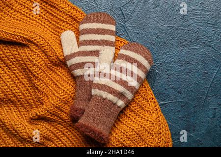 Paar warme Fäustlinge und Kleidung auf dunklem Hintergrund, Nahaufnahme Stockfoto