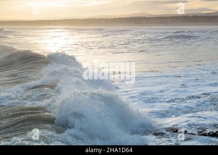 LOSSIEMOUTH, MORAY, SCHOTTLAND - 9. DEZEMBER 2021: Dies ist eine Szene am östlichen Strandbereich des Hafens mit Wellen kurz nach Sonnenaufgang in Lossiemouth, Mo Stockfoto