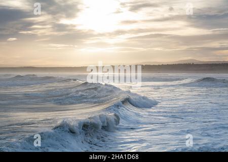 LOSSIEMOUTH, MORAY, SCHOTTLAND - 9. DEZEMBER 2021: Dies ist eine Szene am östlichen Strandbereich des Hafens mit Wellen kurz nach Sonnenaufgang in Lossiemouth, Mo Stockfoto