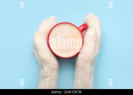 Weibliche Hände in gestrickten Fäustlingen und Tasse leckeren Kakao auf farbigem Hintergrund, Nahaufnahme Stockfoto