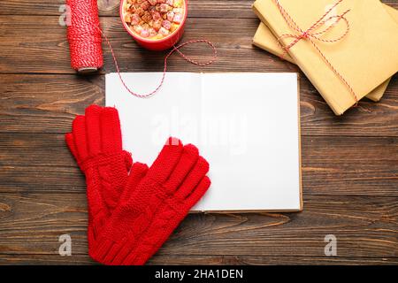 Offenes Buch und warme Handschuhe auf Holzhintergrund. Hallo Winter Stockfoto
