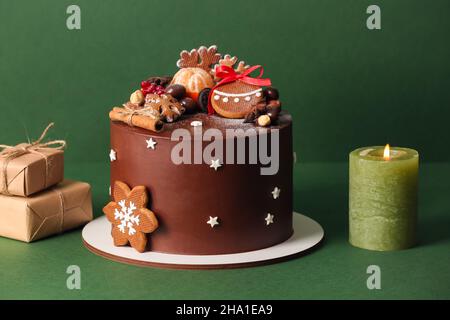 Stand mit leckeren Weihnachts-Schokoladenkuchen und Kerze auf grünem Hintergrund Stockfoto