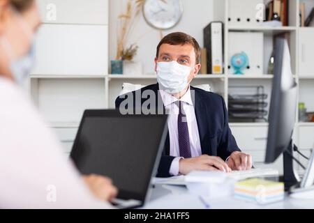 Direktor und Sekretärin in Schutzmasken arbeiten im Büro Stockfoto